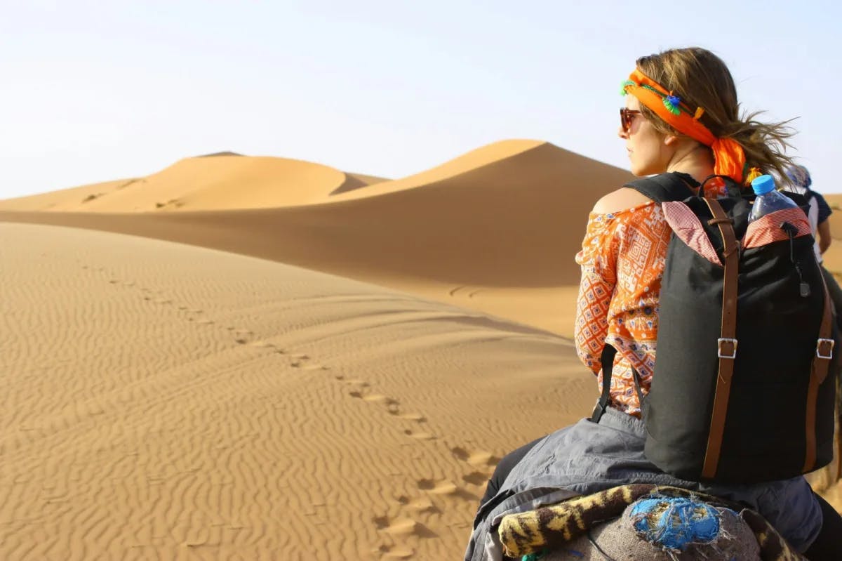 A woman in vibrant attire rides an unseen camel through the plain sands of the Sahara Desert