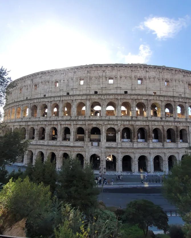 View of the Colosseum in Rome on a sunny day surrounded by trees 