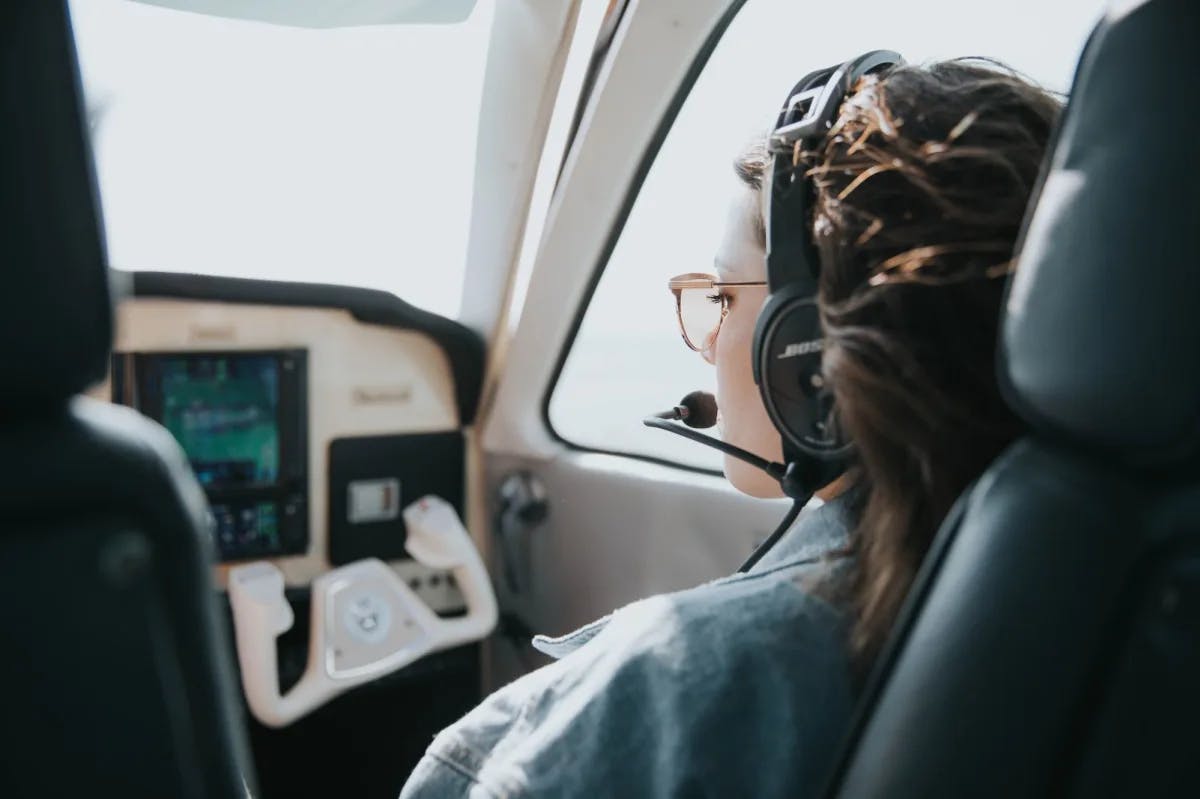 A woman with a pilot's headset sits in the cockpit of a private plane preparing for takeoff