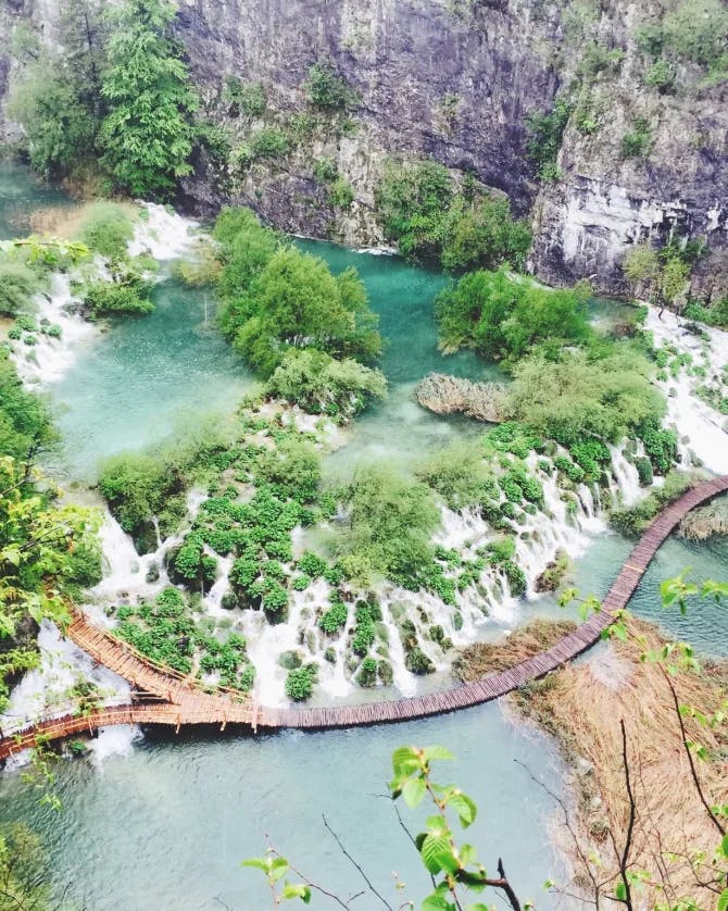 An aerial view of Plitvice Lakes National Park with trees, water and a wooden bridge in the middle