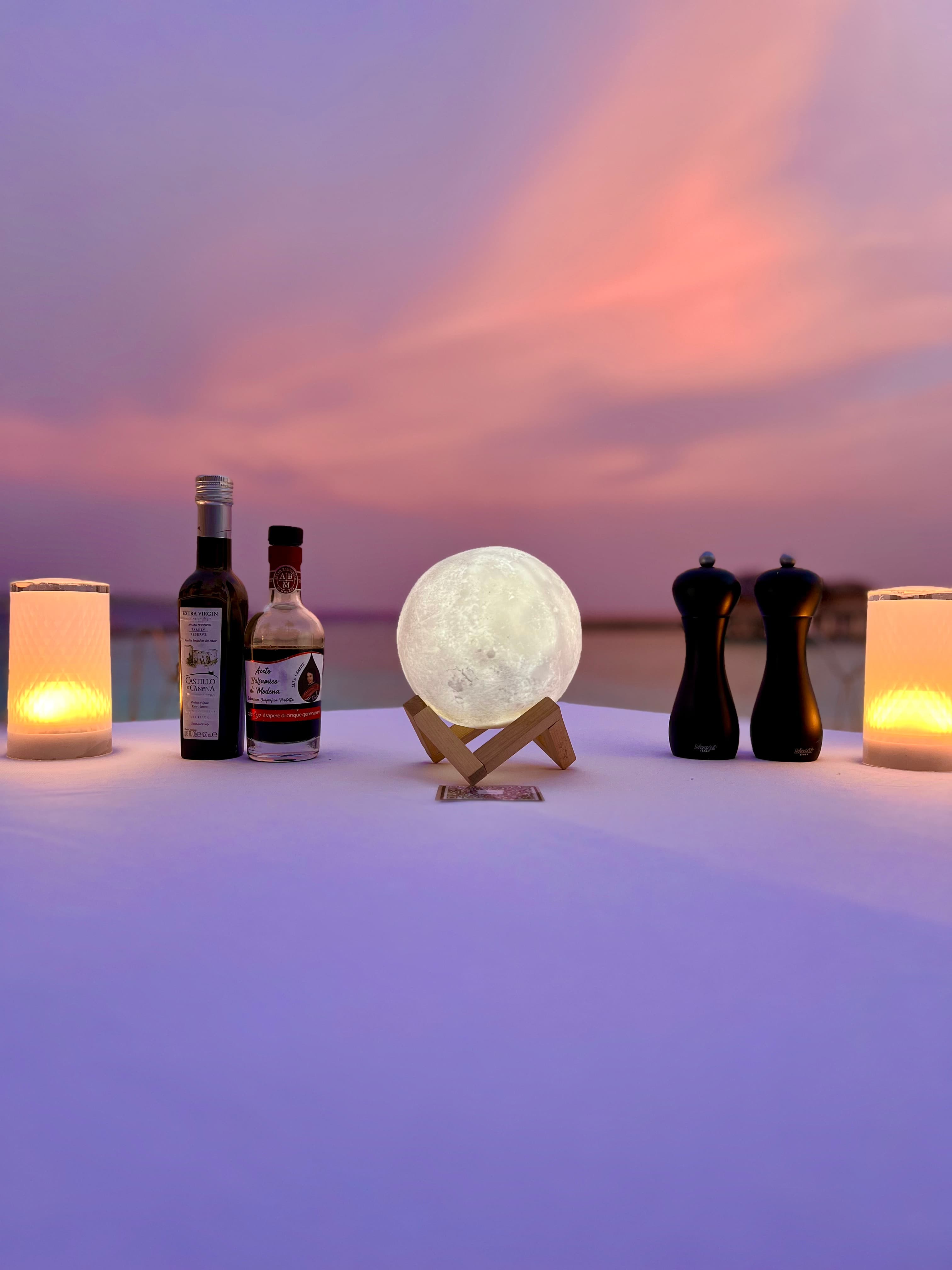 A dining table set-up with a crystal salt lamp, salt and pepper shakers and candles under a pink and purple sunset