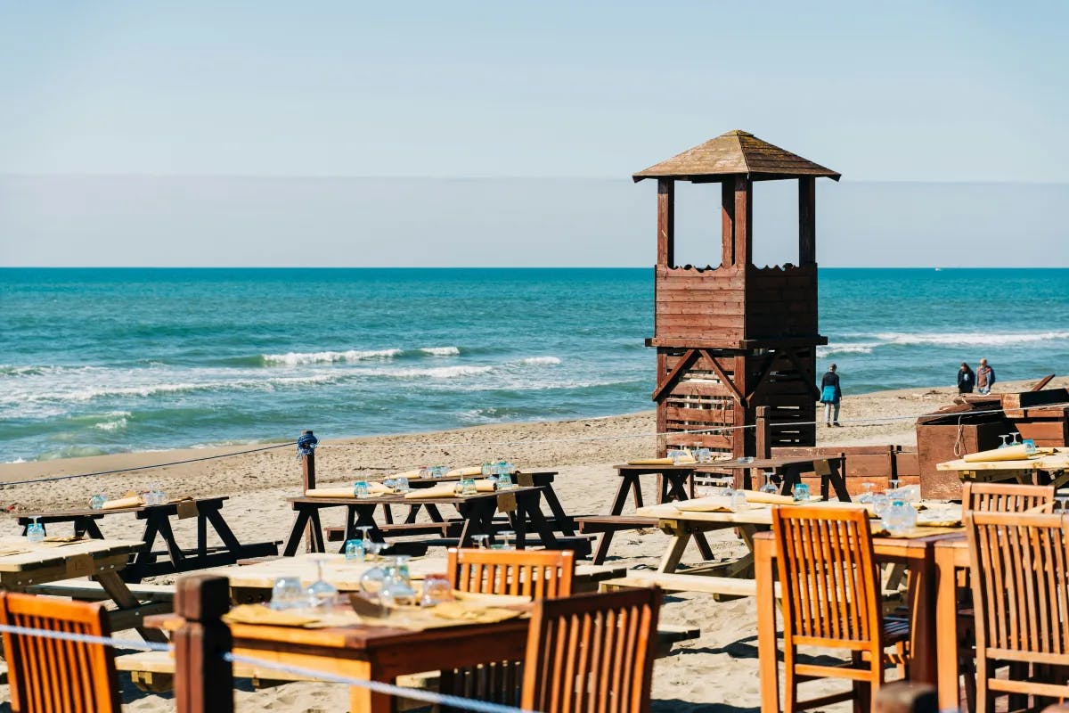 A picture of outdoor restaurant with wooden table and chairs near the beach.