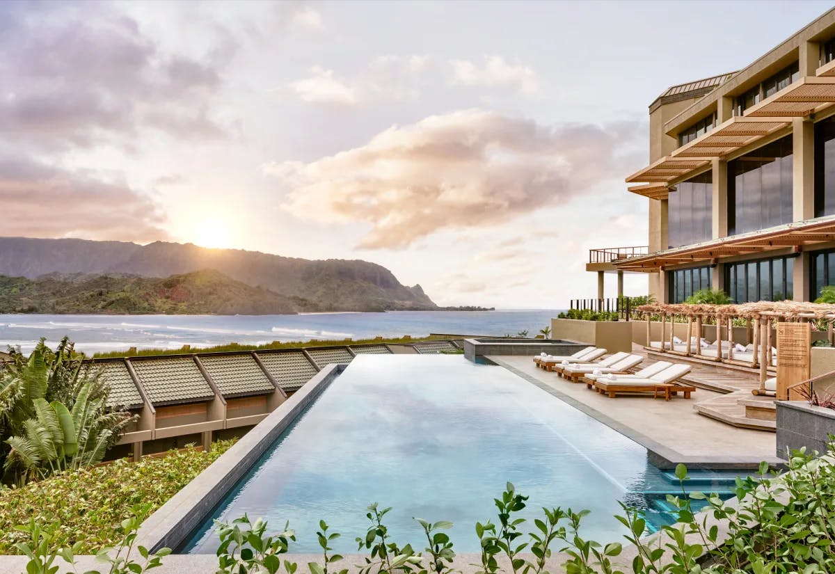 a modern multi-story building with large windows overlooking a sleek infinity pool near the ocean