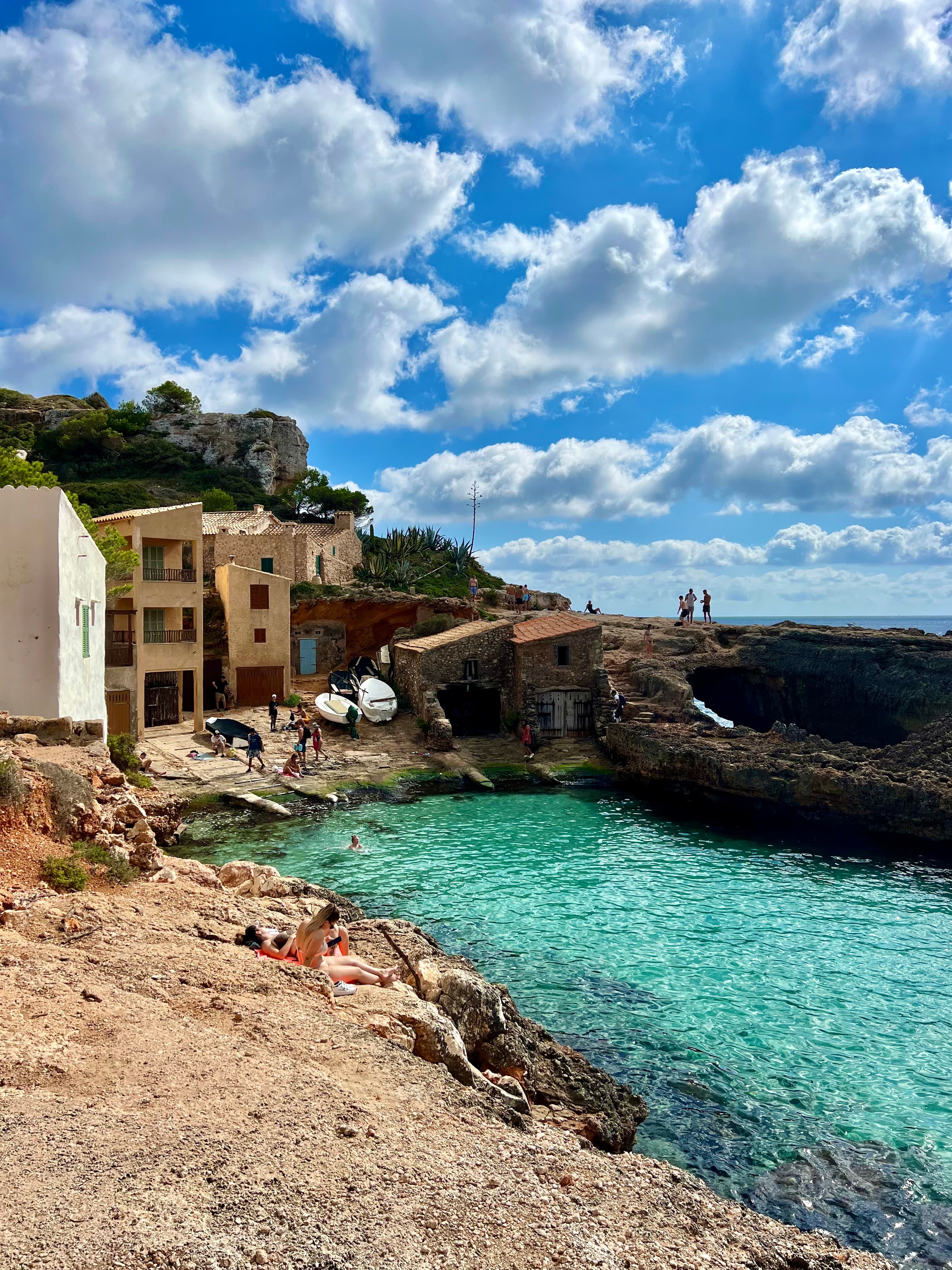 Small intimate beach, with clear, azure water next to small, stone houses.