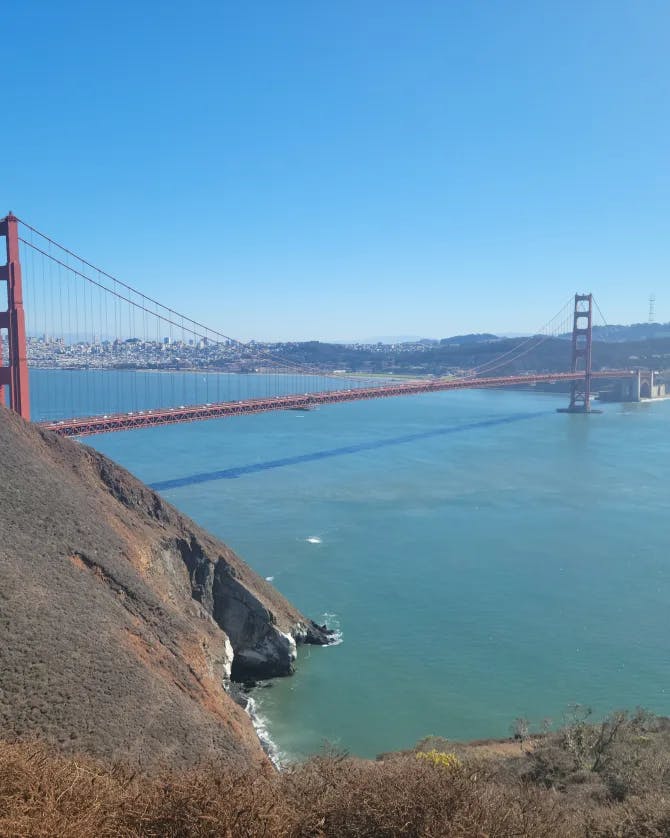 A picture of the Golden Gate Bridge over the blue water with land in the forefront and background