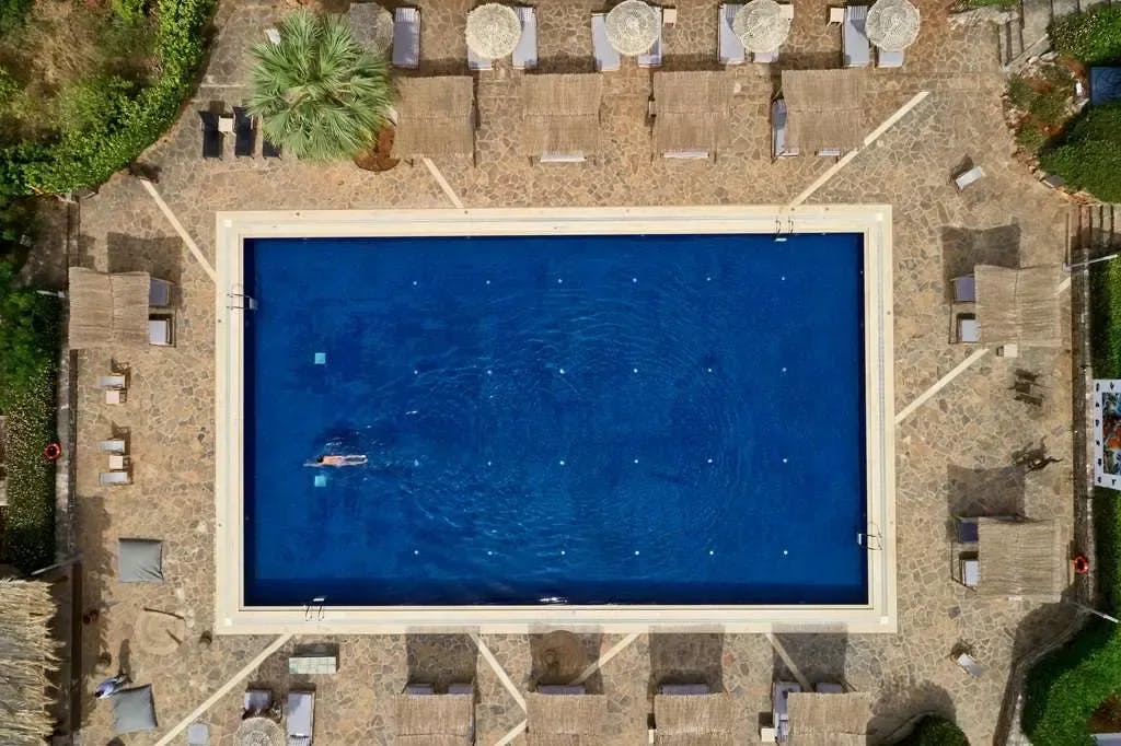 A lone swimmer strokes through a sapphire-blue pool surrounded by luxe loungers at Minos Beach Art Hotel in Crete