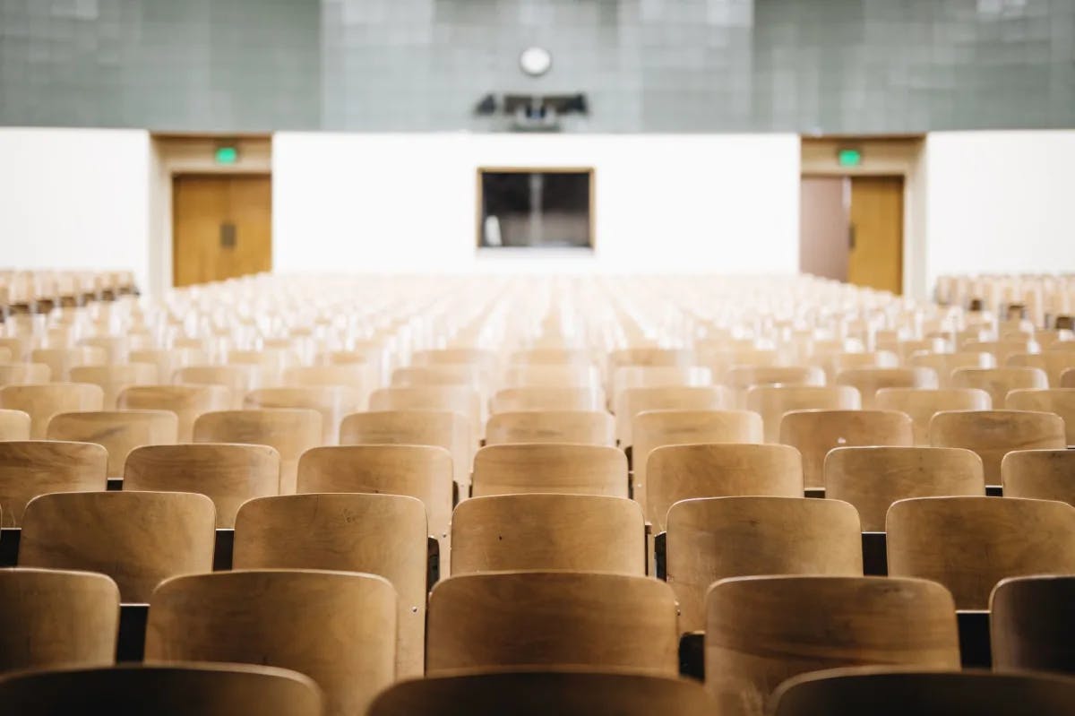 Rows of utilitarian classroom seats sit empty in a drab auditorium