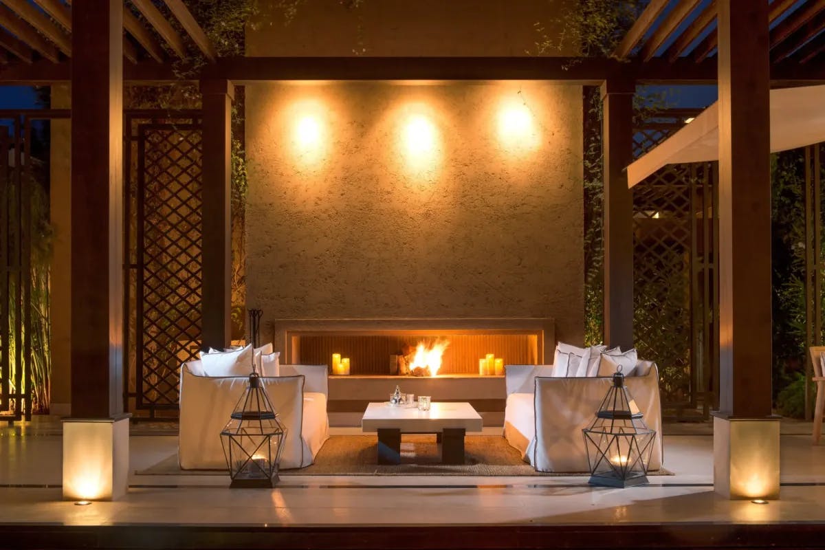 An outdoor lounge area lit by a large fireplace and hosting plush sofas and ornate lanterns