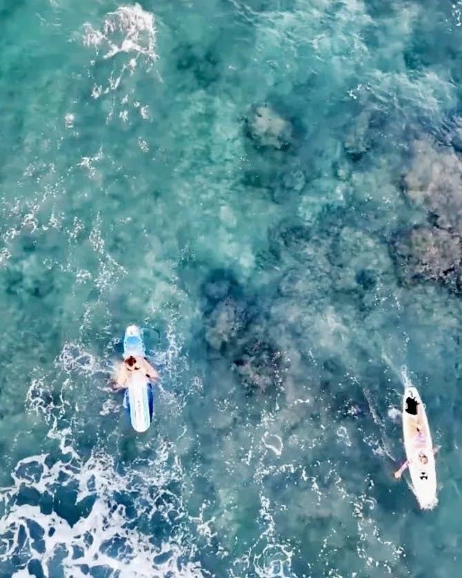 An aerial view of two people surfing over turquoise blue water