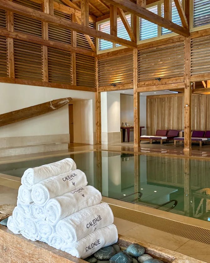 White towels rolled up near a swimming pool inside of a wooden building with ceiling beams