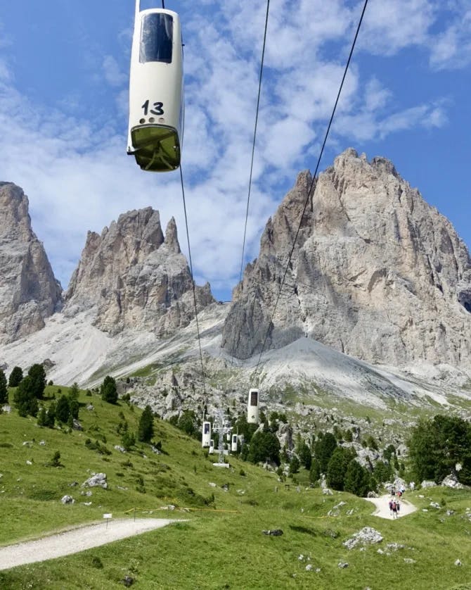 A cable car at Forcella del Sassolungo above green rolling hills toward a rocky mountain