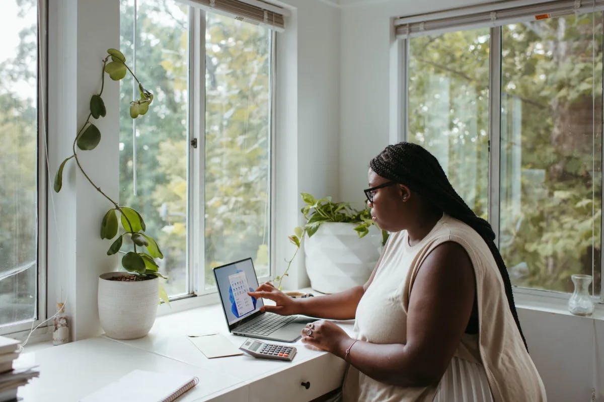 A woman works on her laptop at contemporary desk with lovely house plants and greenery outside
