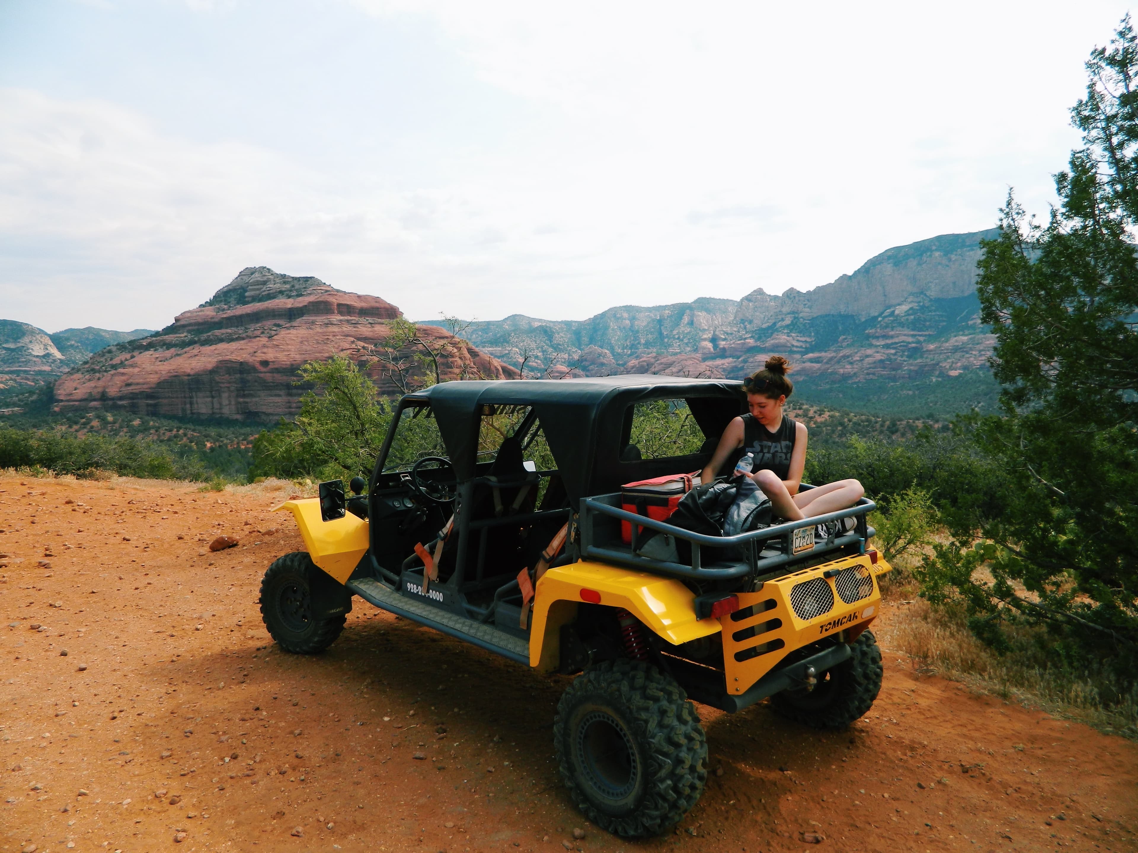 Alyssa sitting in the back of an open Jeep in the desert with open areas and trees.