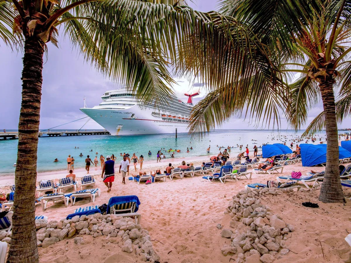 A picture of people on the beach with a cruise on the water during the daytime.