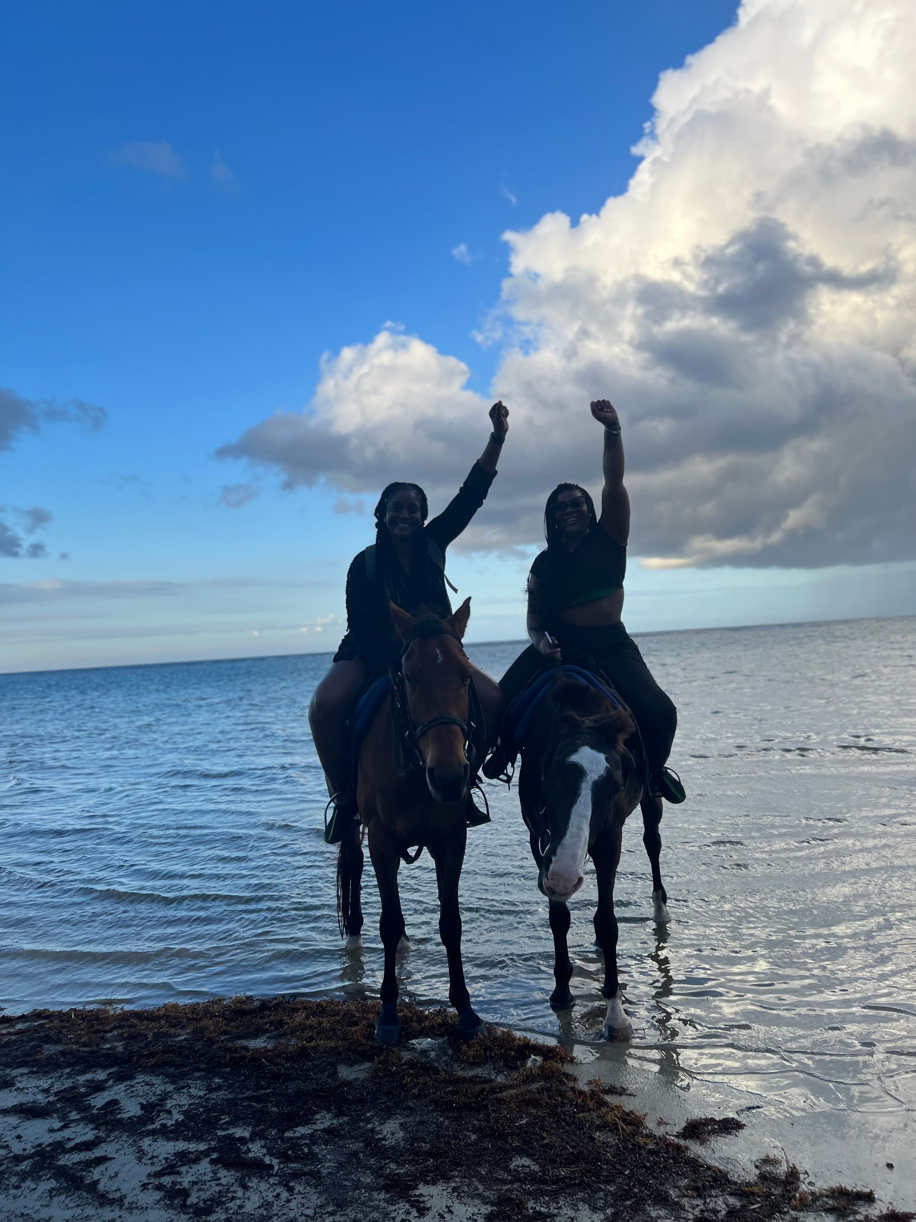 Two people riding horses on the ocean shore.