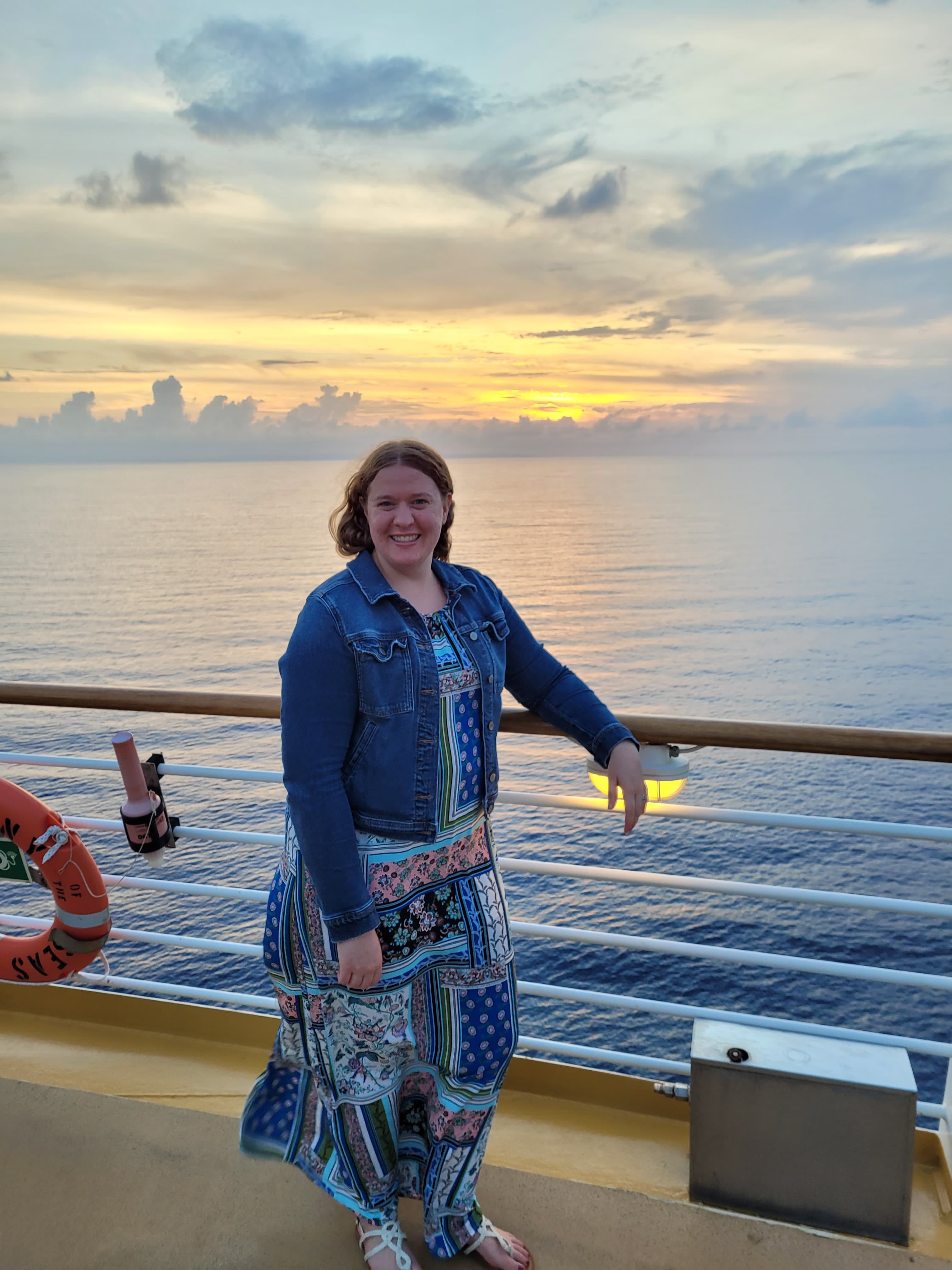 Sea bound Stephanie standing on the deck of a ship, with a soft breeze, before a whimsical sunset.