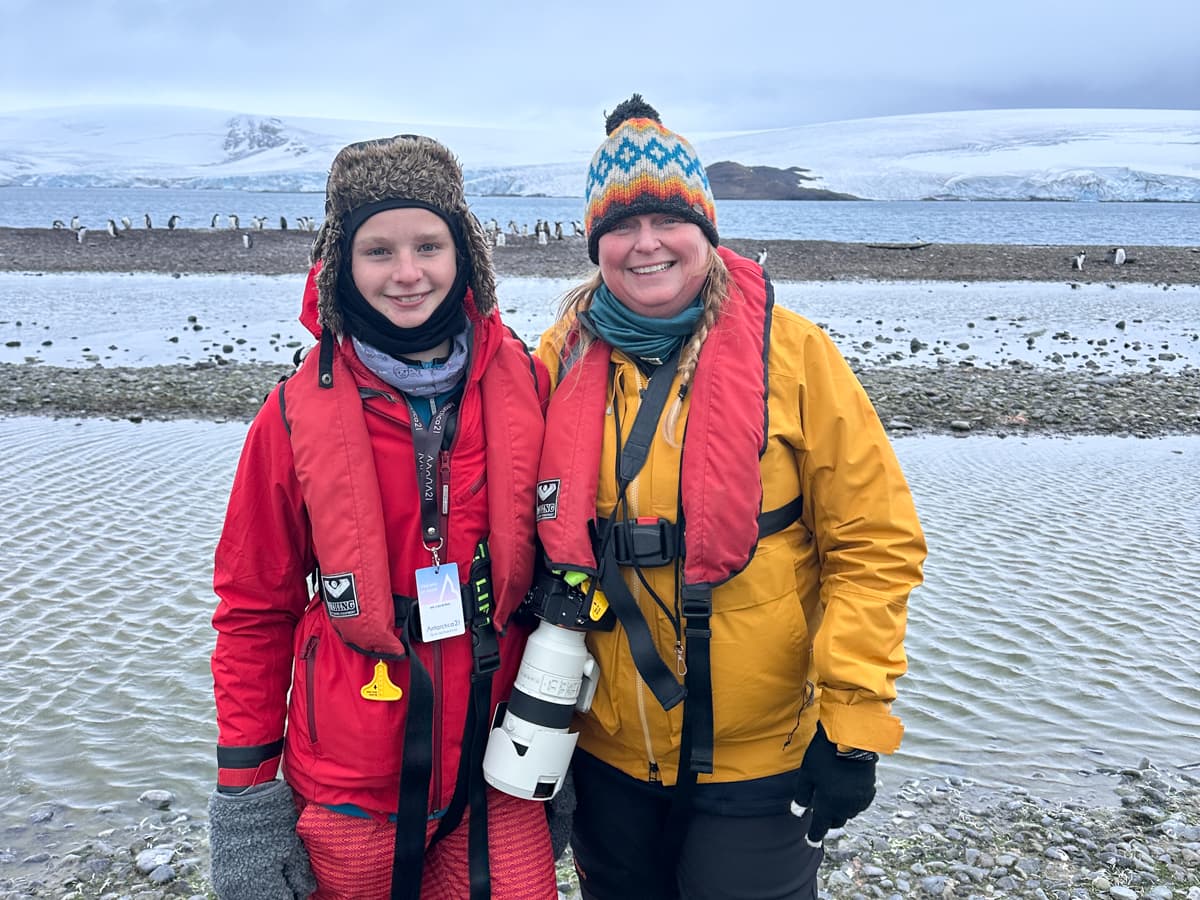 Karilyn and her son smiling for a photo with penguins in the background.
