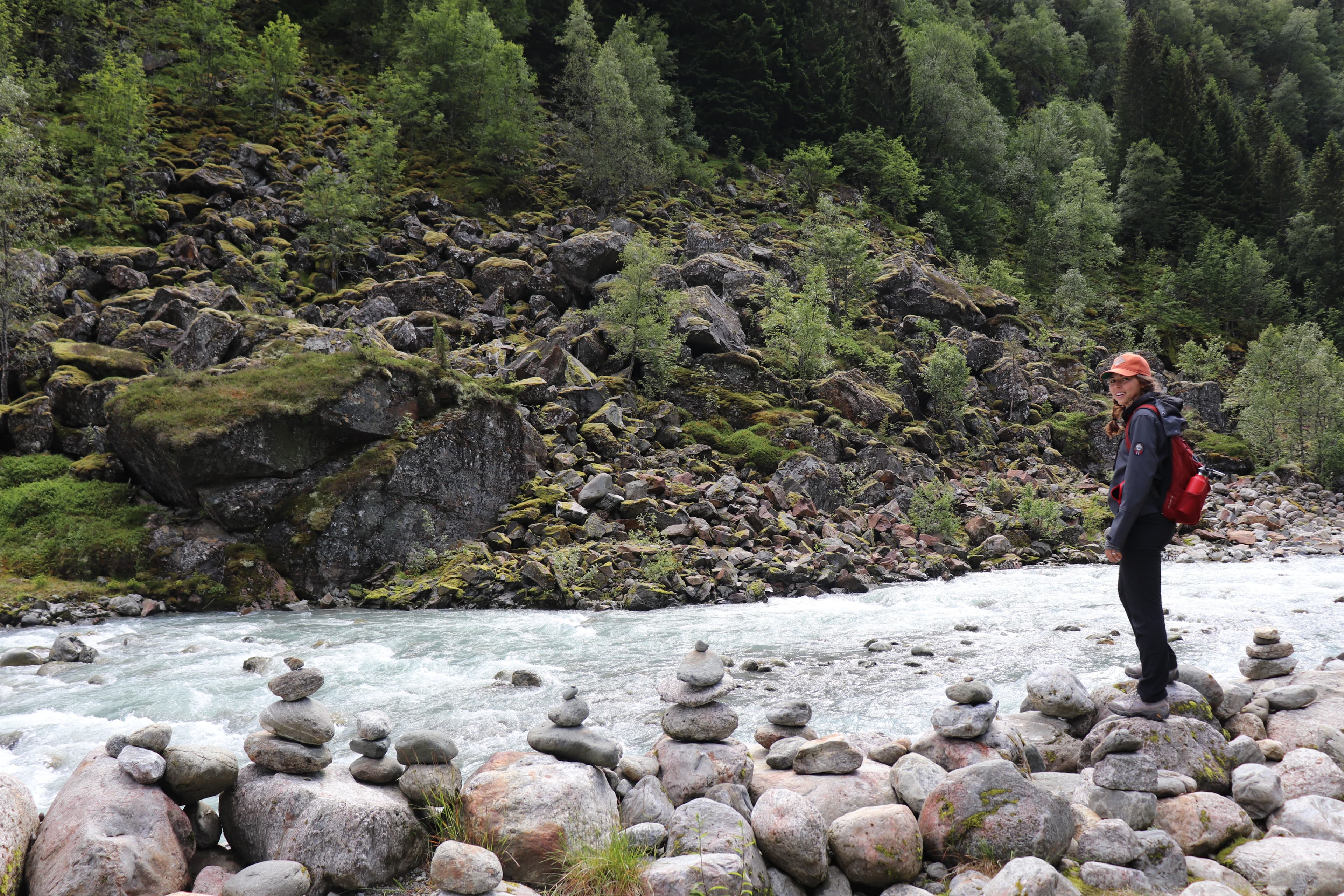 Emily standing on a rock near a river with boulders and green trees in the background.