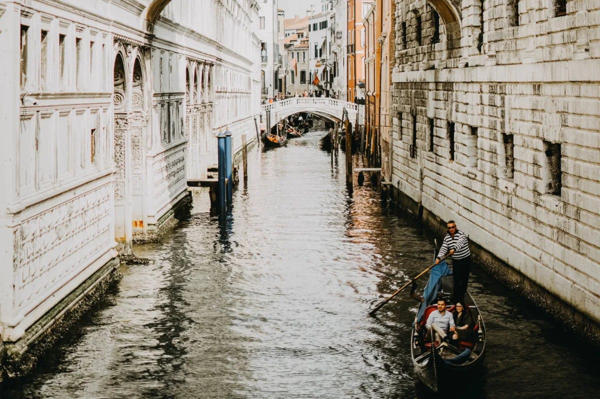 People riding gondola in city canal between buildings.