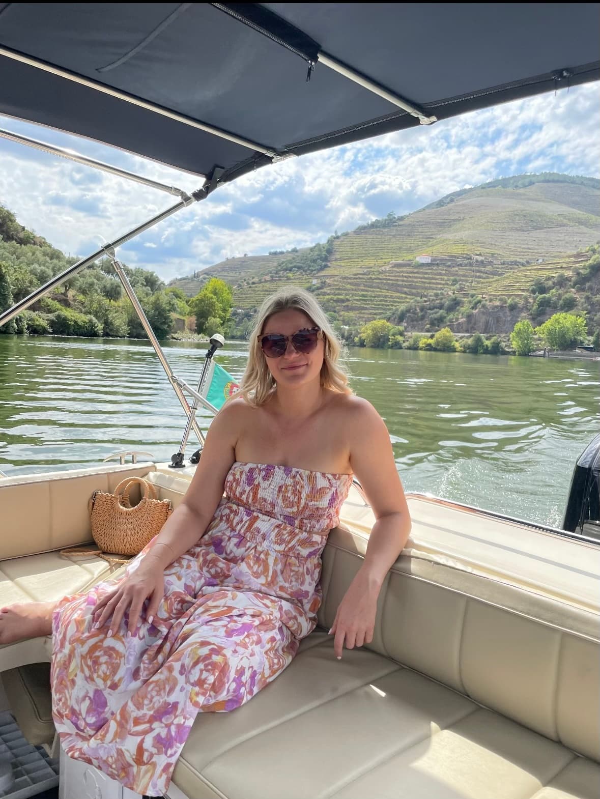 Picture of Ashley sitting on a boat, wearing a colorful dress with the water and mountain in the background