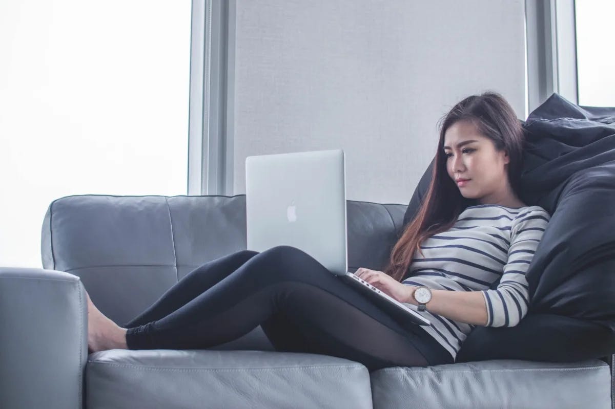 A woman lying on a comfy-looking couch while working on her laptop