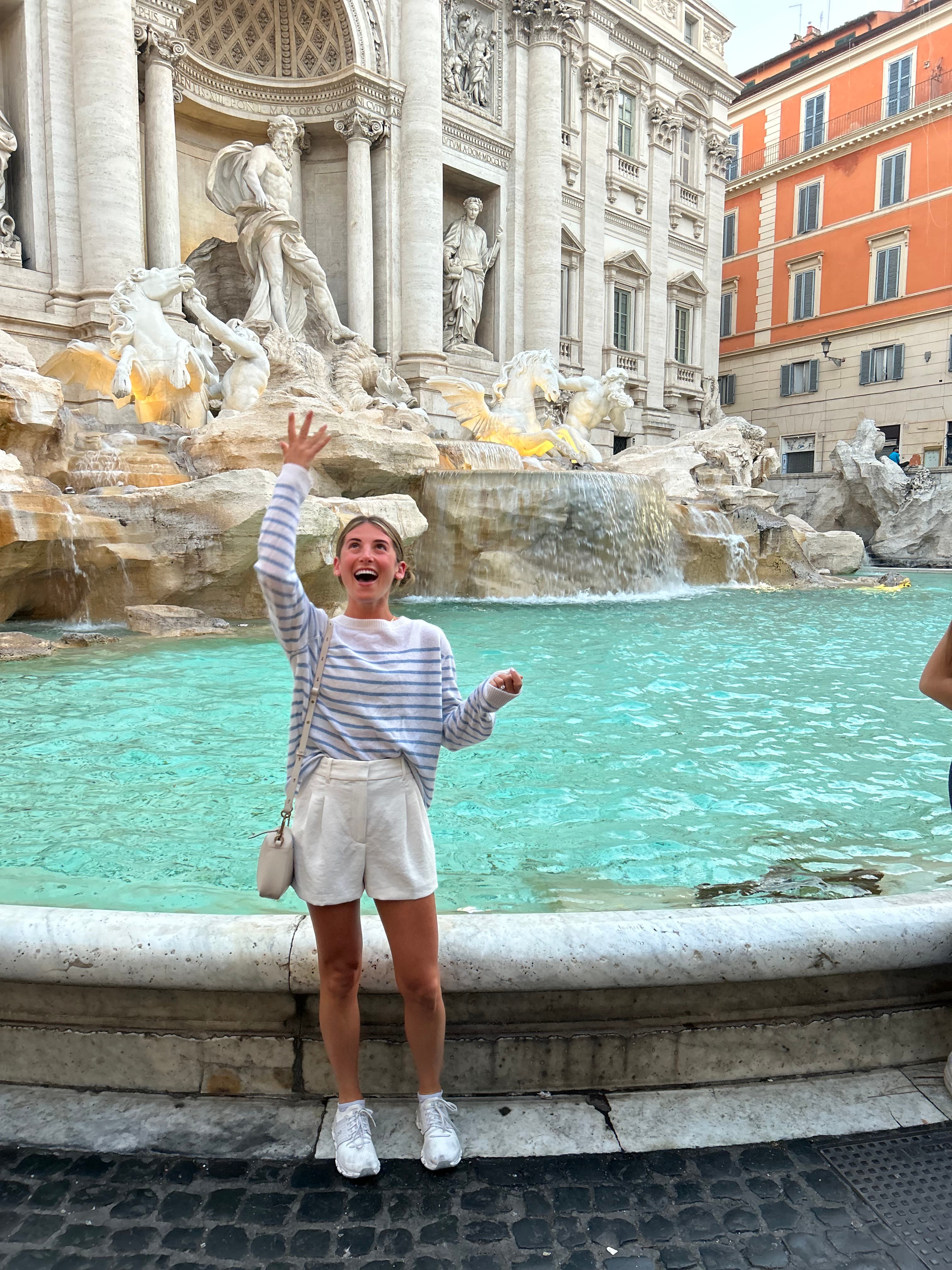 Picture of Shelby throwing a coin into the Trevi fountain while wearing a striped top and white shorts