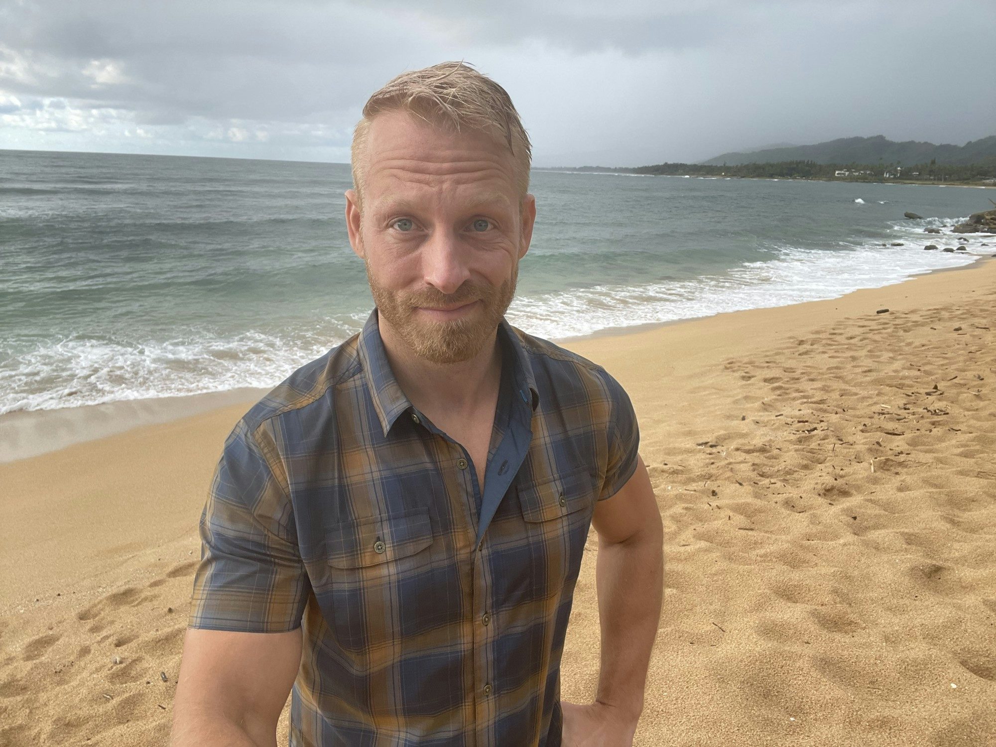 Travel Advisor Andrew Bergeron stands on a beach wearing a blue and brown plaid shirt