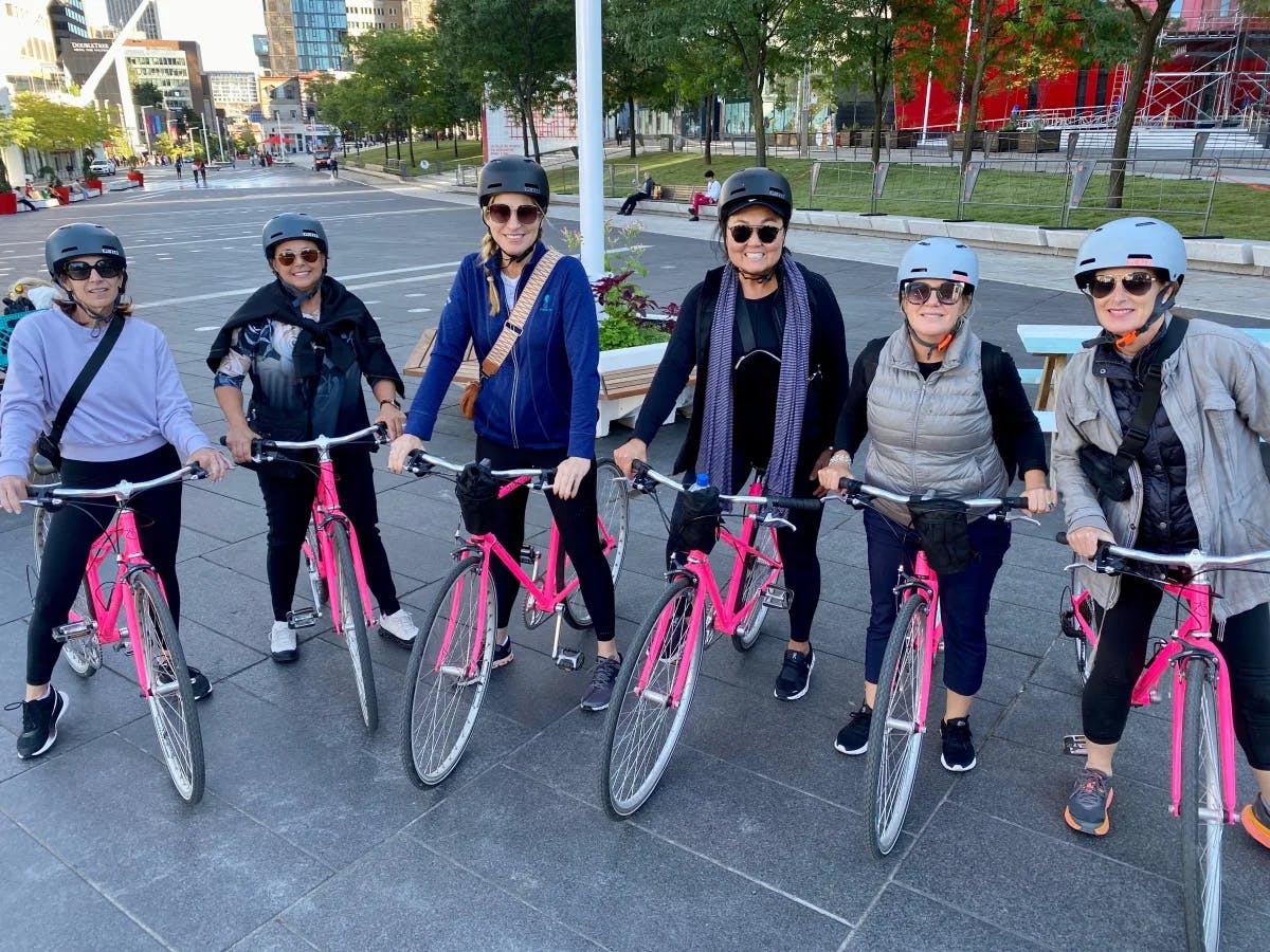 A group of people each on top of a pink bicycle with helmets on outside.