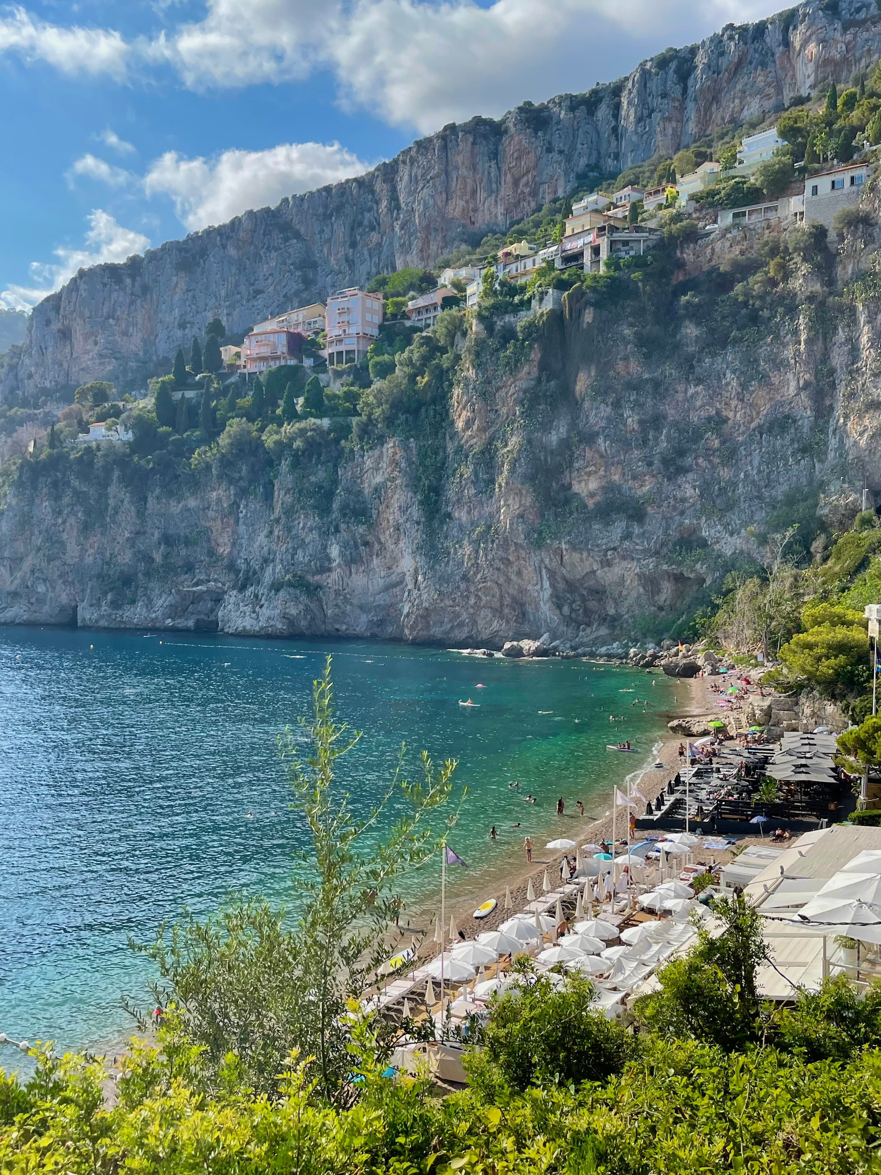 A photo of a rocky cliff looking down onto a beach, trees and blue water