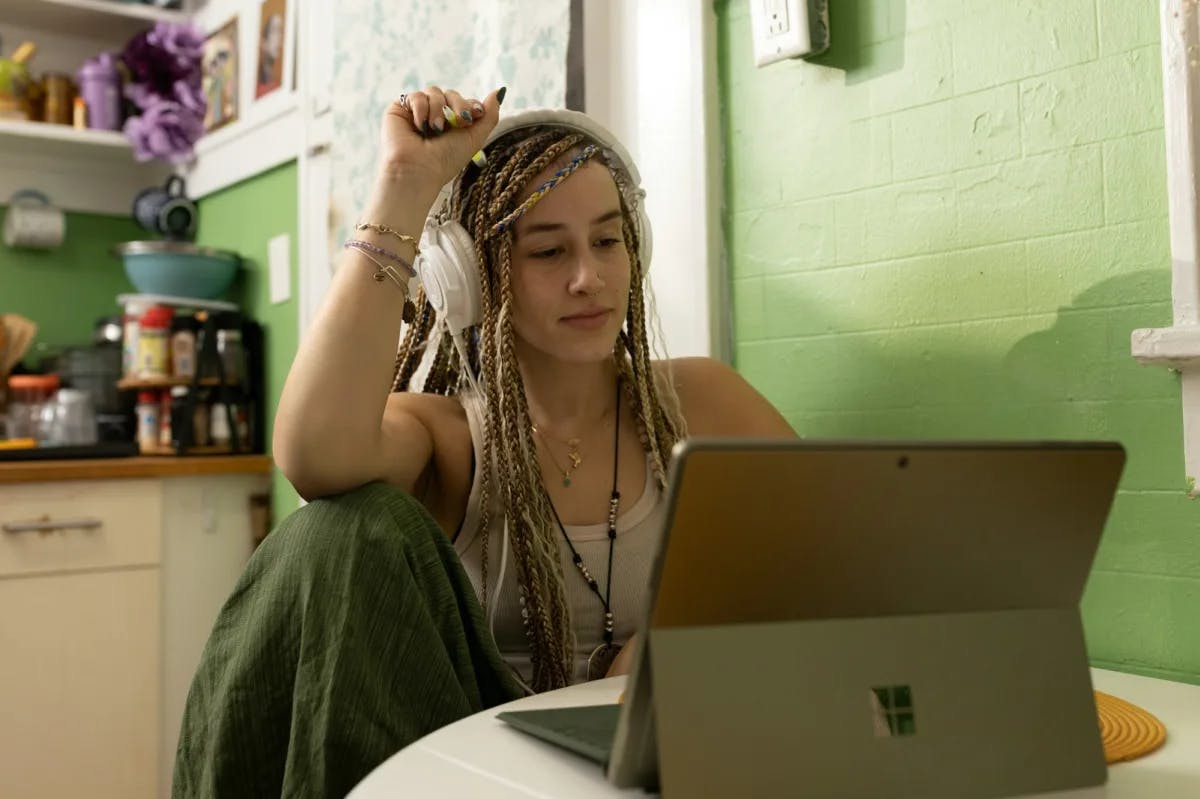 From home, a woman with dreadlocks and pro headphones takes courses on her laptop