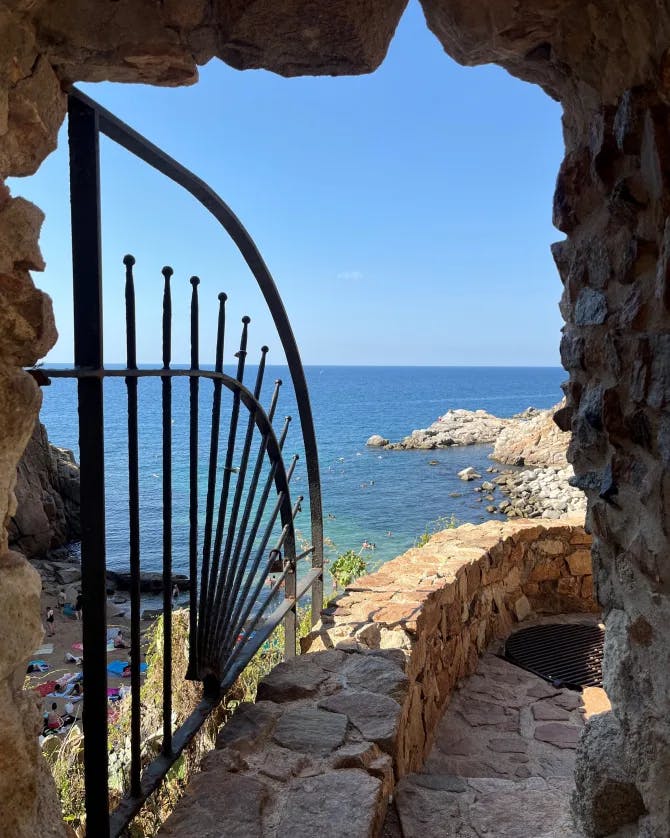 A view of Tossa de Mar Spain behind a metal gate with the blue sea in the background.
