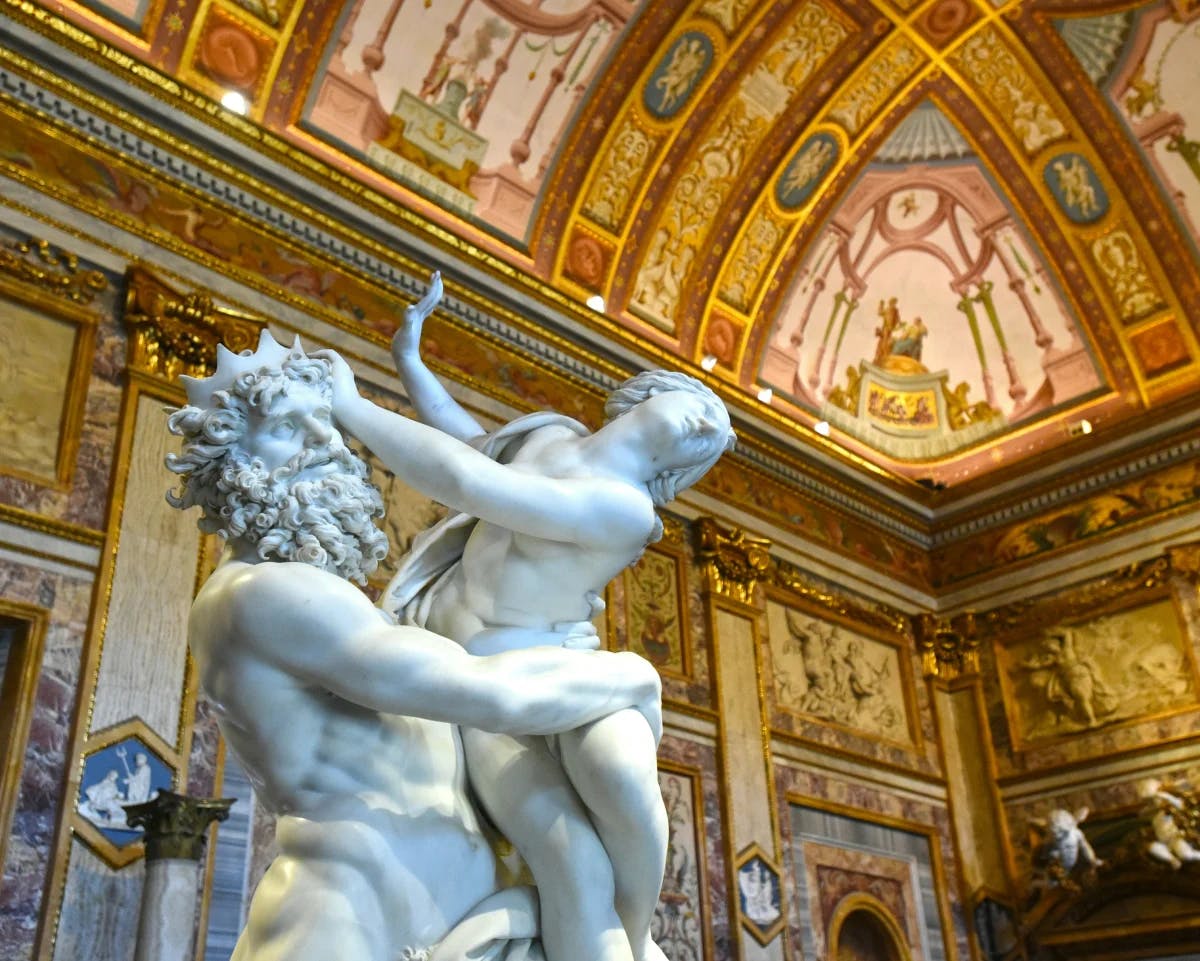 Sculptures in the Galeria Borghese with an ornately painted gold roof above them.