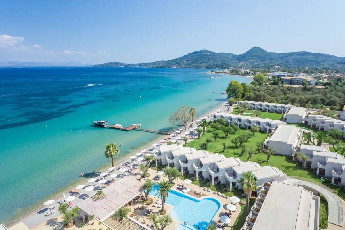 The shoreline of Corfu takes center stage, with sapphire waves turning turquoise in the shallows and whitewashed resort buildings lining the beaches