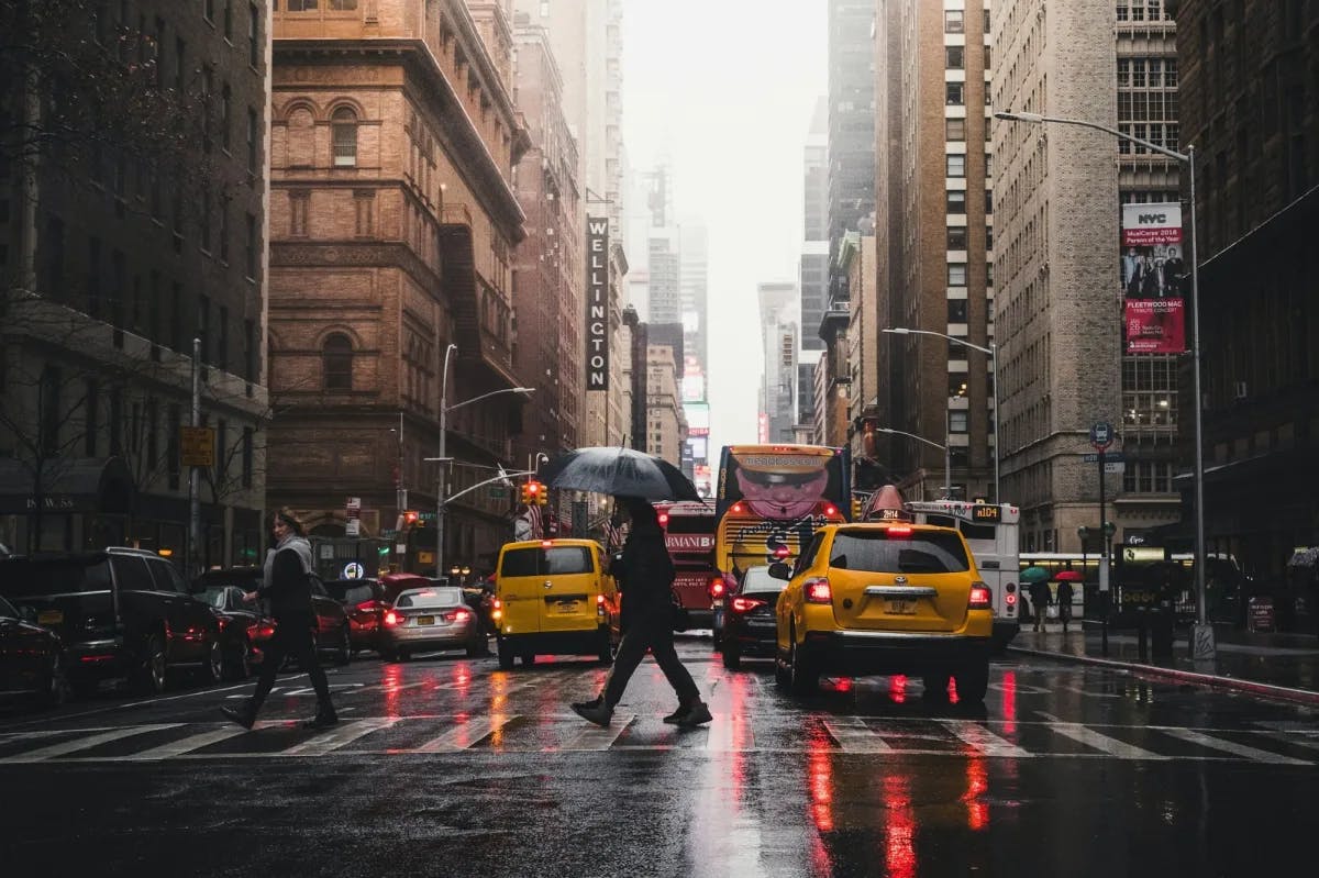 On a cold, rainy day in Manhattan, travelers and heavy traffic cross a street
