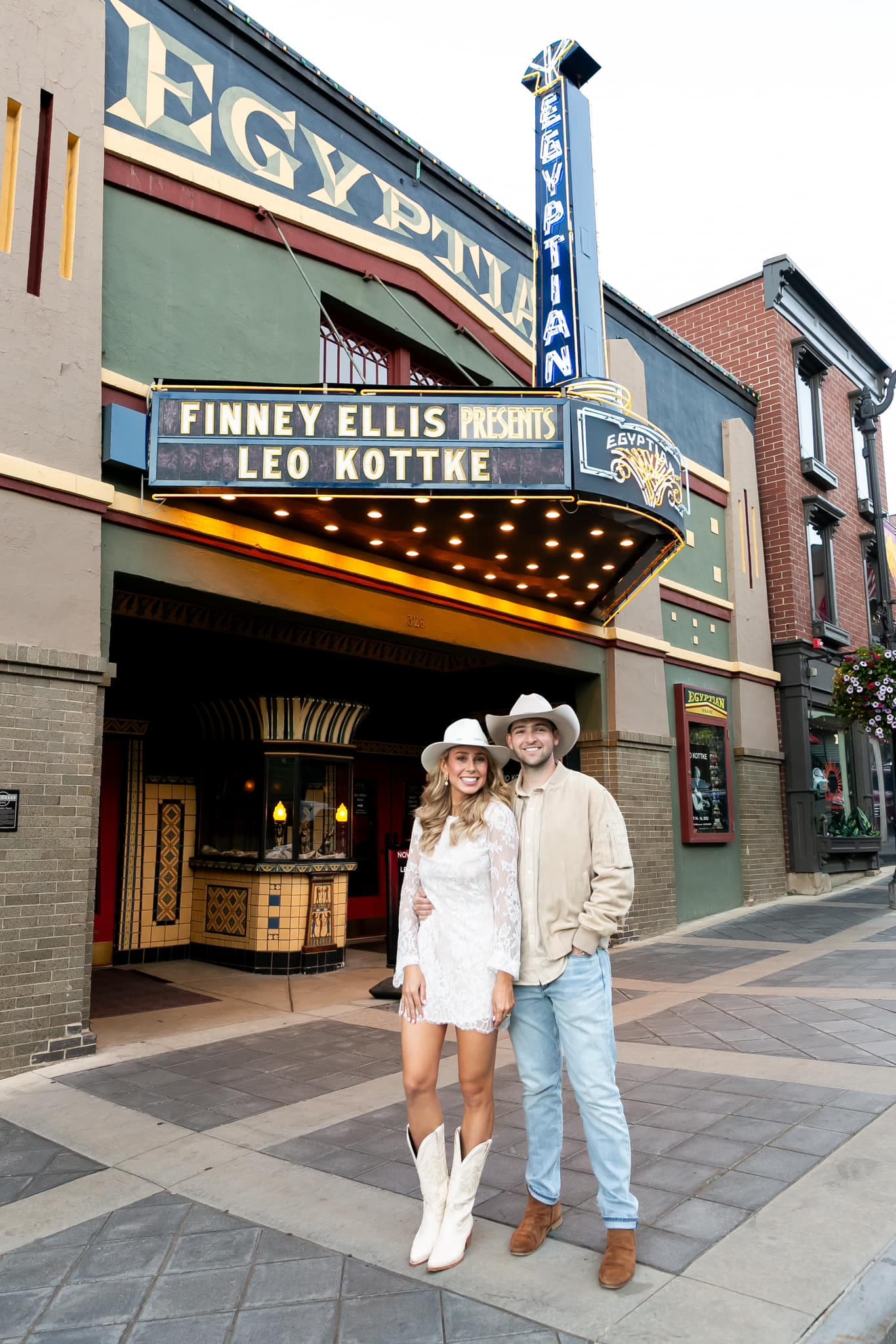Couple posing in front of an old movie theater, wearing cowboy hats.