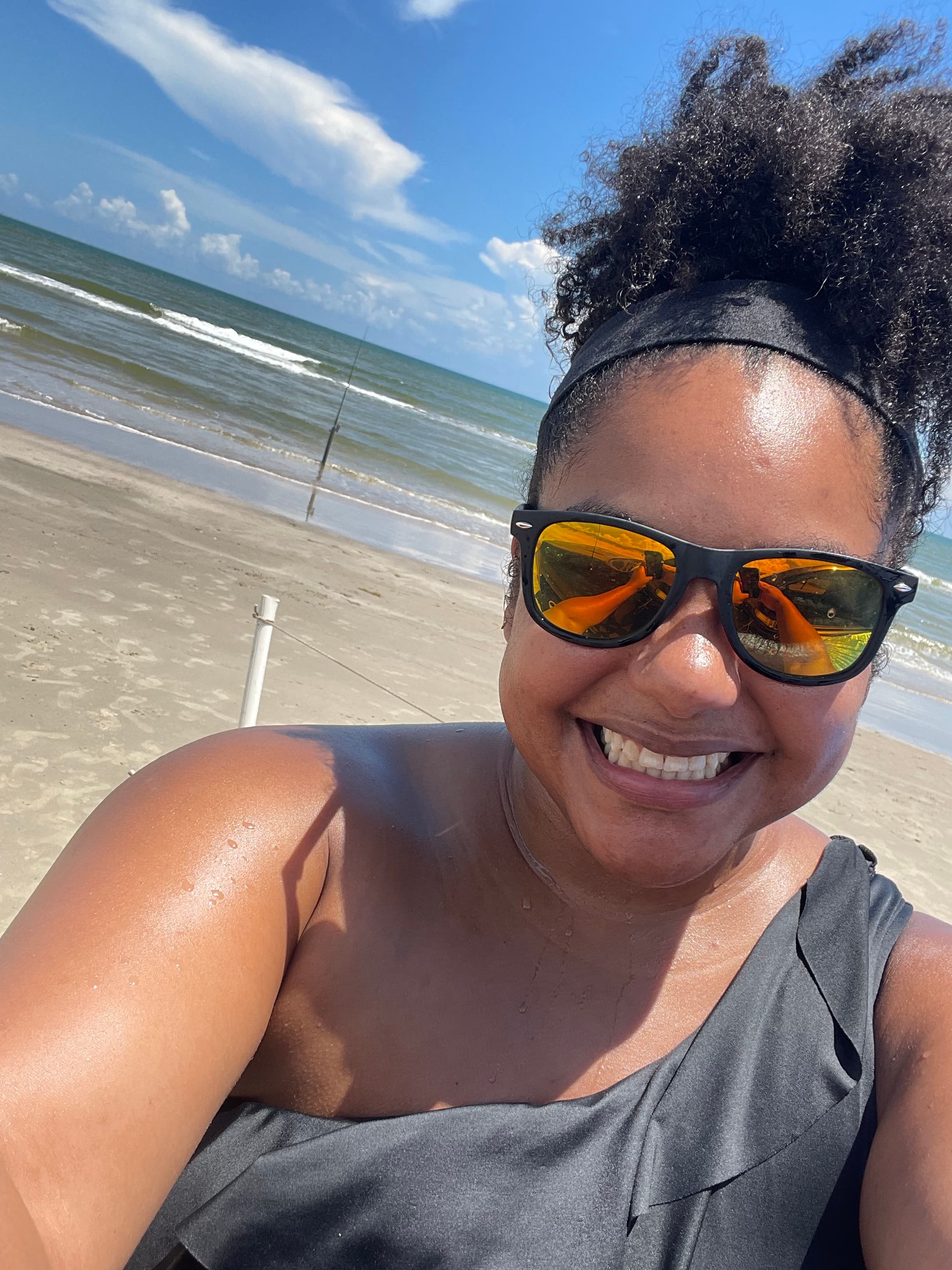 Big selfie smile on the beach with mild waves and blue skies with a few fun clouds.