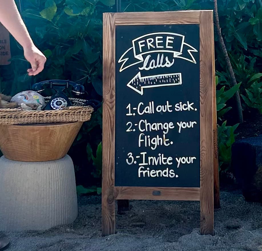 A chalk board that reads 'free calls' with a telephone on a table next to it