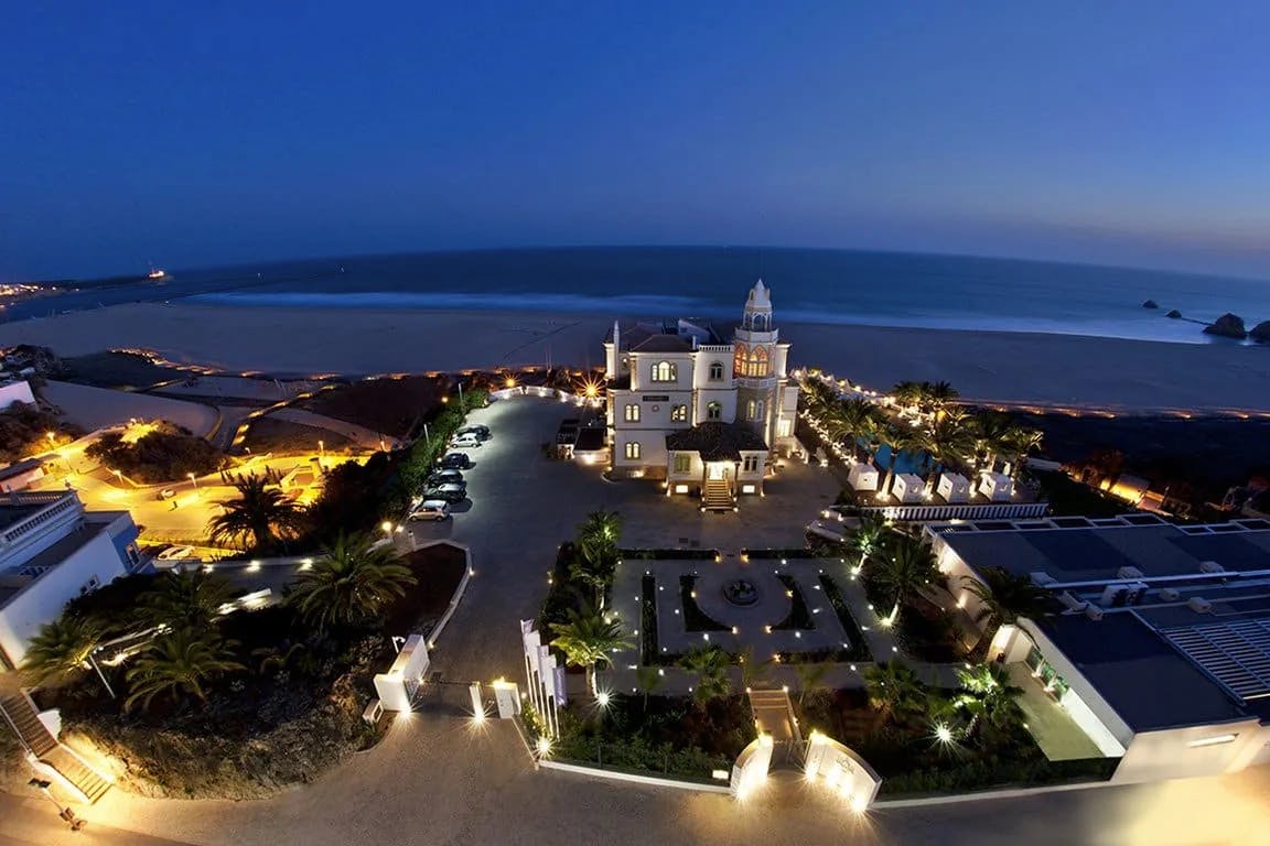 A nighttime aerial view of Bela Vista Hotel & Spa, showing the hotel and its grounds lit up with the beach in the distance