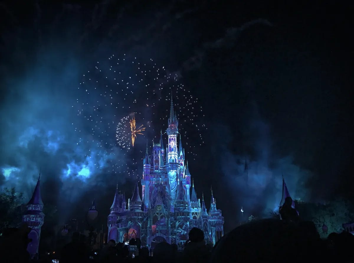 A view of the stunning castle at Disney World with fireworks and colorful lights lit up. 