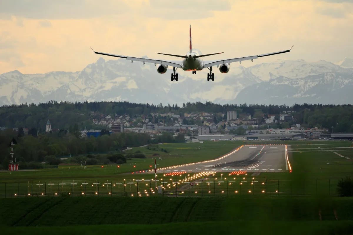 A passenger jet is about to touch down at Zurich airport with the forested skyline in the background distracting from vast mountain views in the far distance