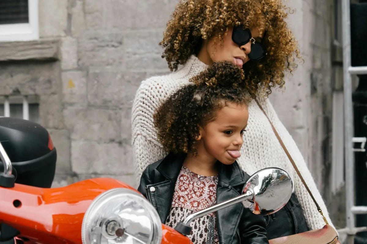 A mom and her young daughter make faces in the rearview mirror of a motorcycle