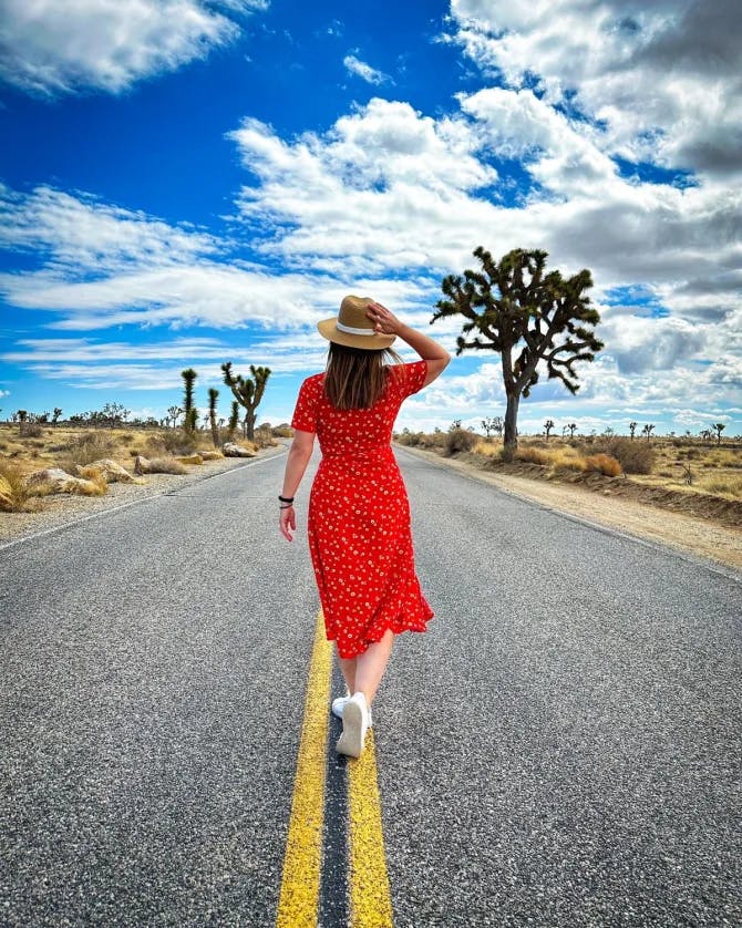 Picture of Marisa on a road in a desert setting with clear skies and trees in the distance. 