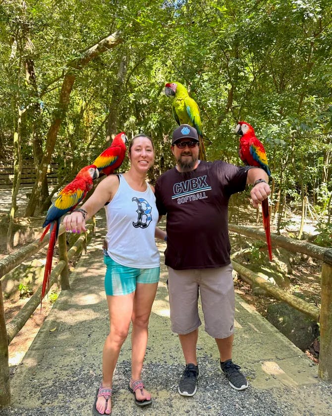 Picture of Amanda and partner holding parrots in front of trees