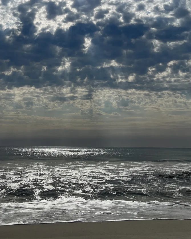 Picture of beach with a cloudy sky and the sun shining through the clouds.