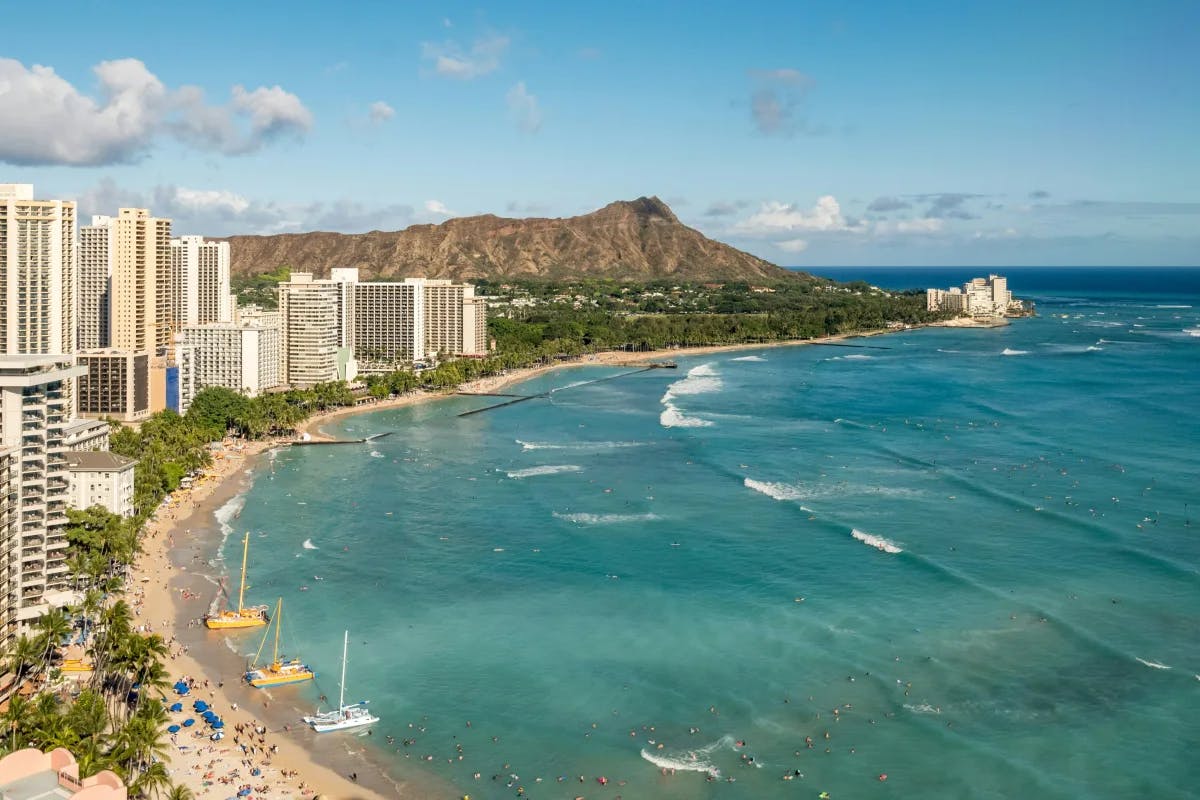 An aerial view of Waikiki Beach with golden sands, hotels along the water and Diamond Head in the background.