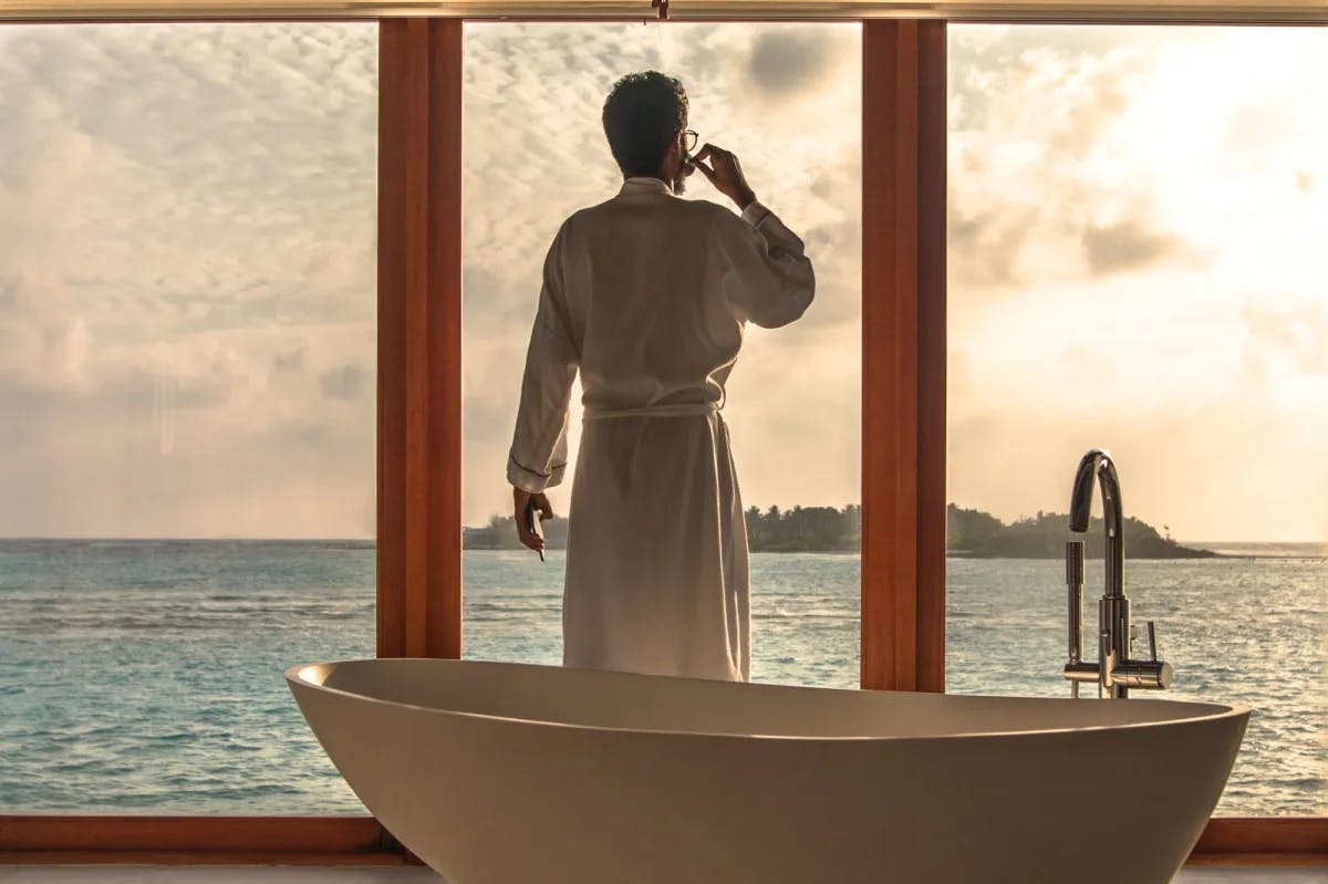 Standing in front of floor-to-ceiling windows, a man in a pristine bathrobe sips an espresso behind a spa tub somewhere in the Maldives