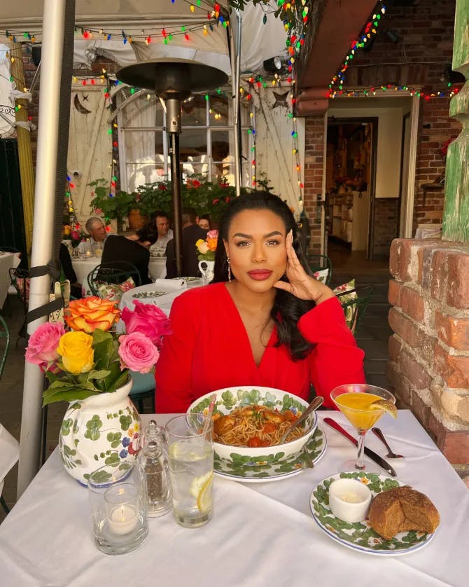 A woman in a red blouse sits at a table with a bowl of soup at a restaurant.