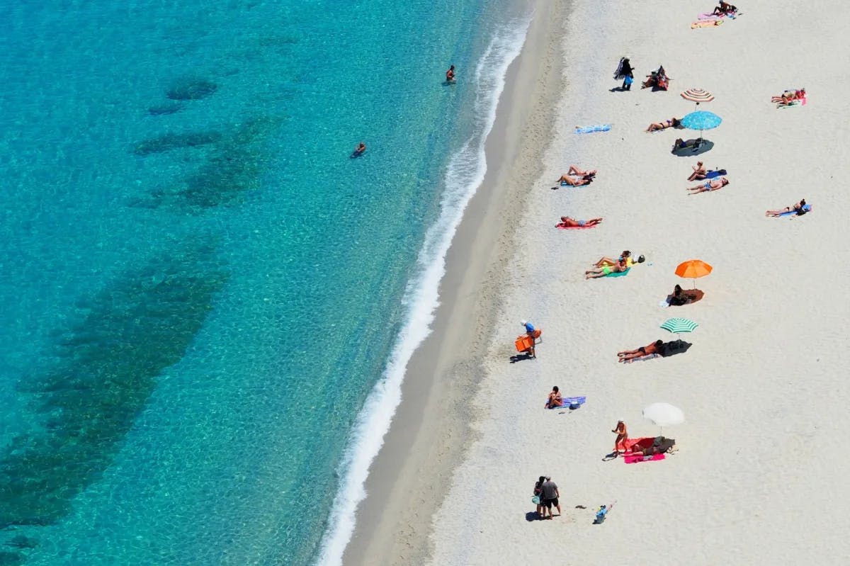 A dozen or so travelers relax on stunning white sands near turquoise-blue water in Tropea, Italy