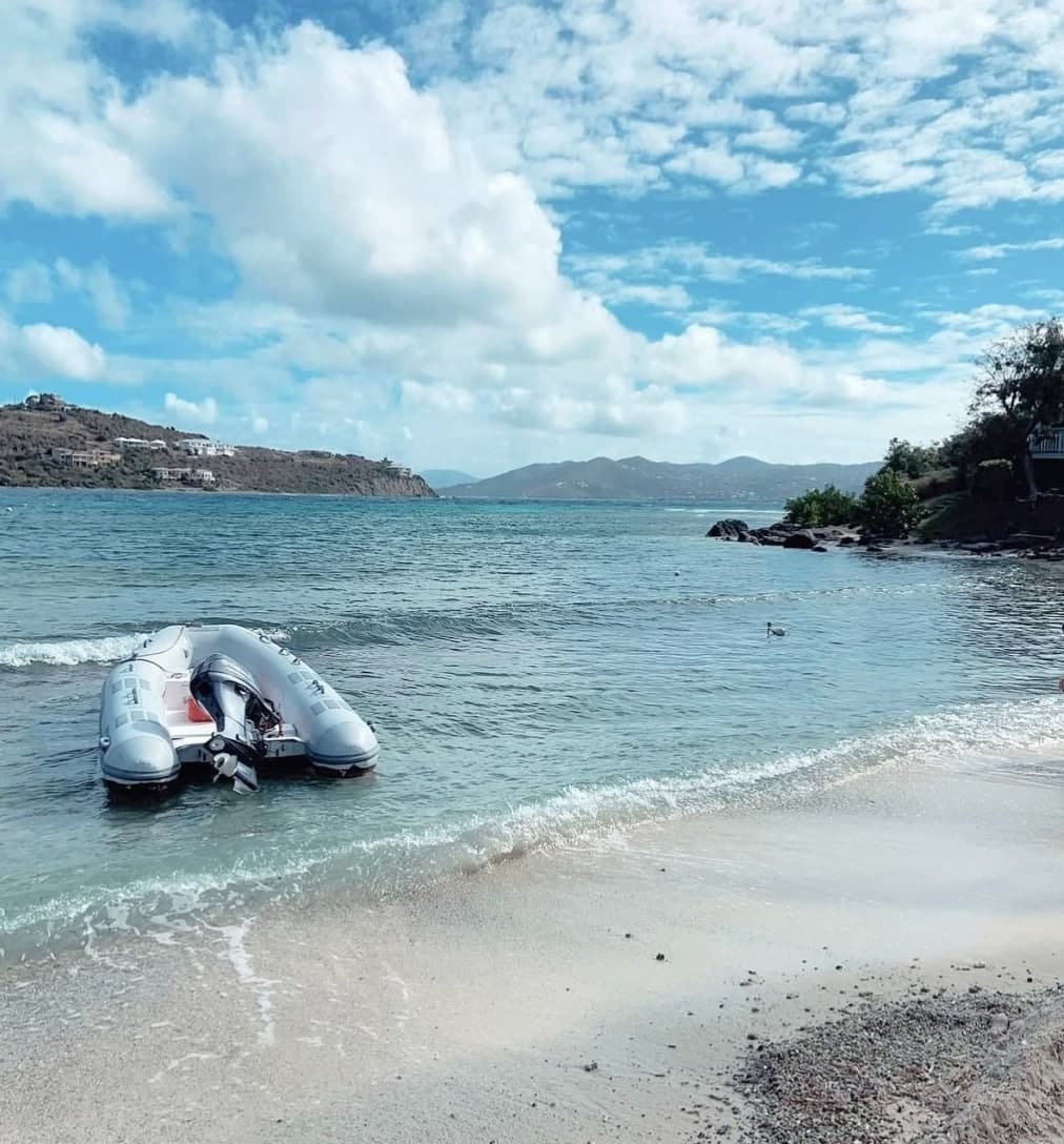 Picture of boat on a shoreline with clear water and foliage in the distance.