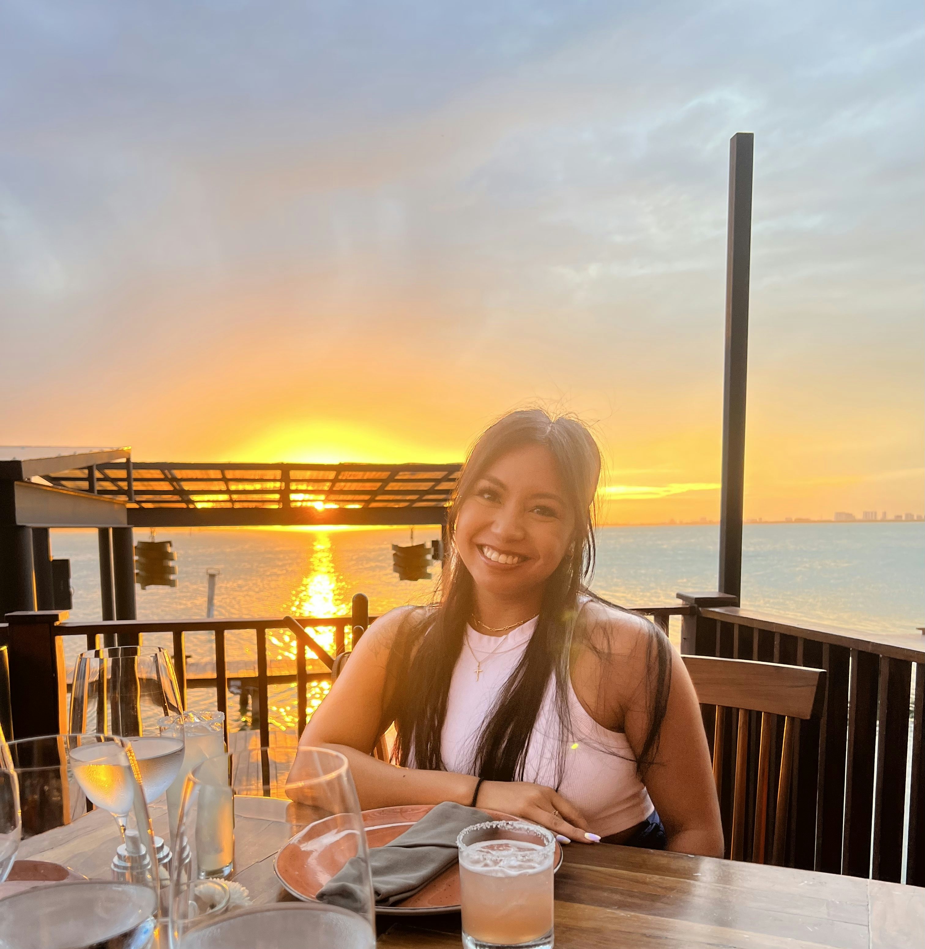 Fora travel agent Kassandra Manalo sitting at table with water and sunset in background
